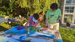 Carol and Katherine in a member's yard painting murals for Homeward House